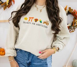 Woman wearing a sweater with 'Thankful for Agriculture' text and fall-themed graphics, standing in a decorated room.